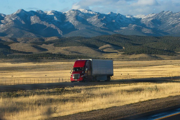 Red semi truck hauling freight through mountain landscape — CDL-A trucking career