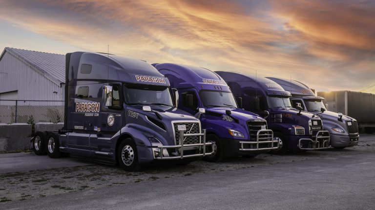 Paragon Freight fleet of Volvo semi-trucks lined up at yard during sunset